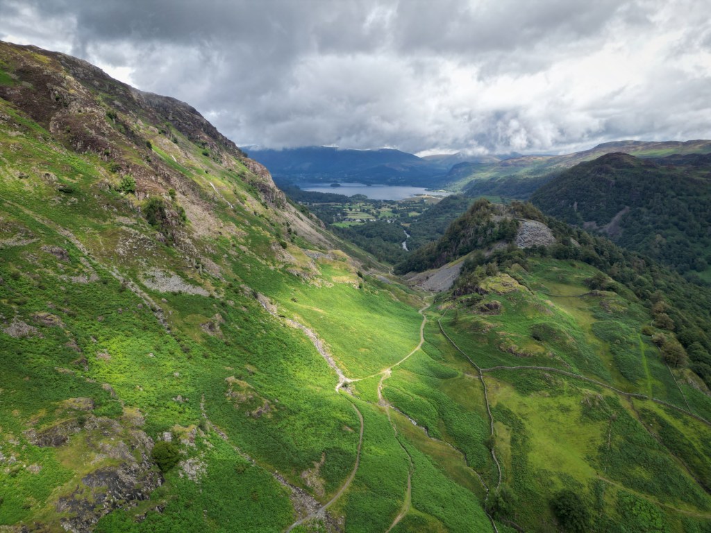Aerial drone photograph of the Lake District mountain landscape, showcasing rugged peaks, valleys, and lakes under natural lighting.