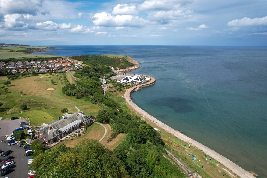 High-resolution aerial photograph of the North Sea coastline at Scarborough, taken by drone on a bright summer day with blue skies and gentle waves.